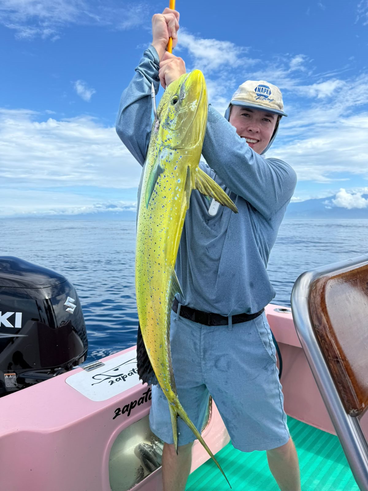 Angler lifting a bright mahi-mahi aboard the pink boat